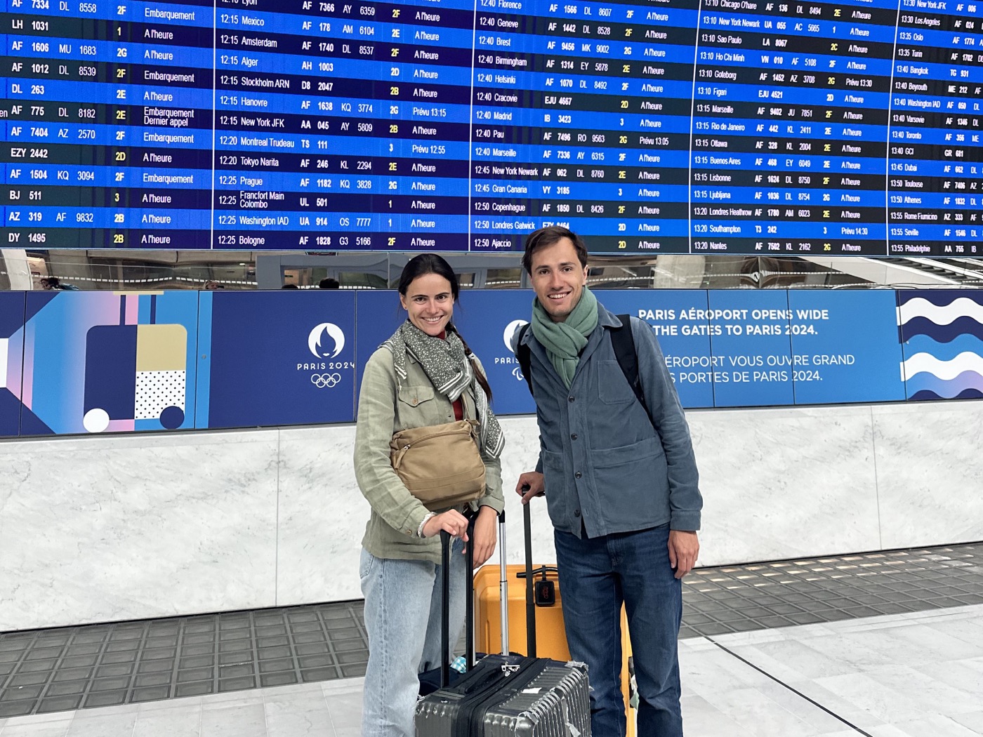 Hélène et Sébastien avec leurs valises devant le tableau des départs